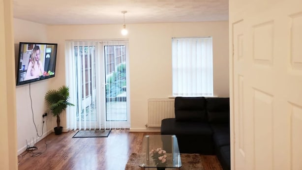 A living room with a black sofa, a glass coffee table, a TV mounted on the wall, and a potted plant.