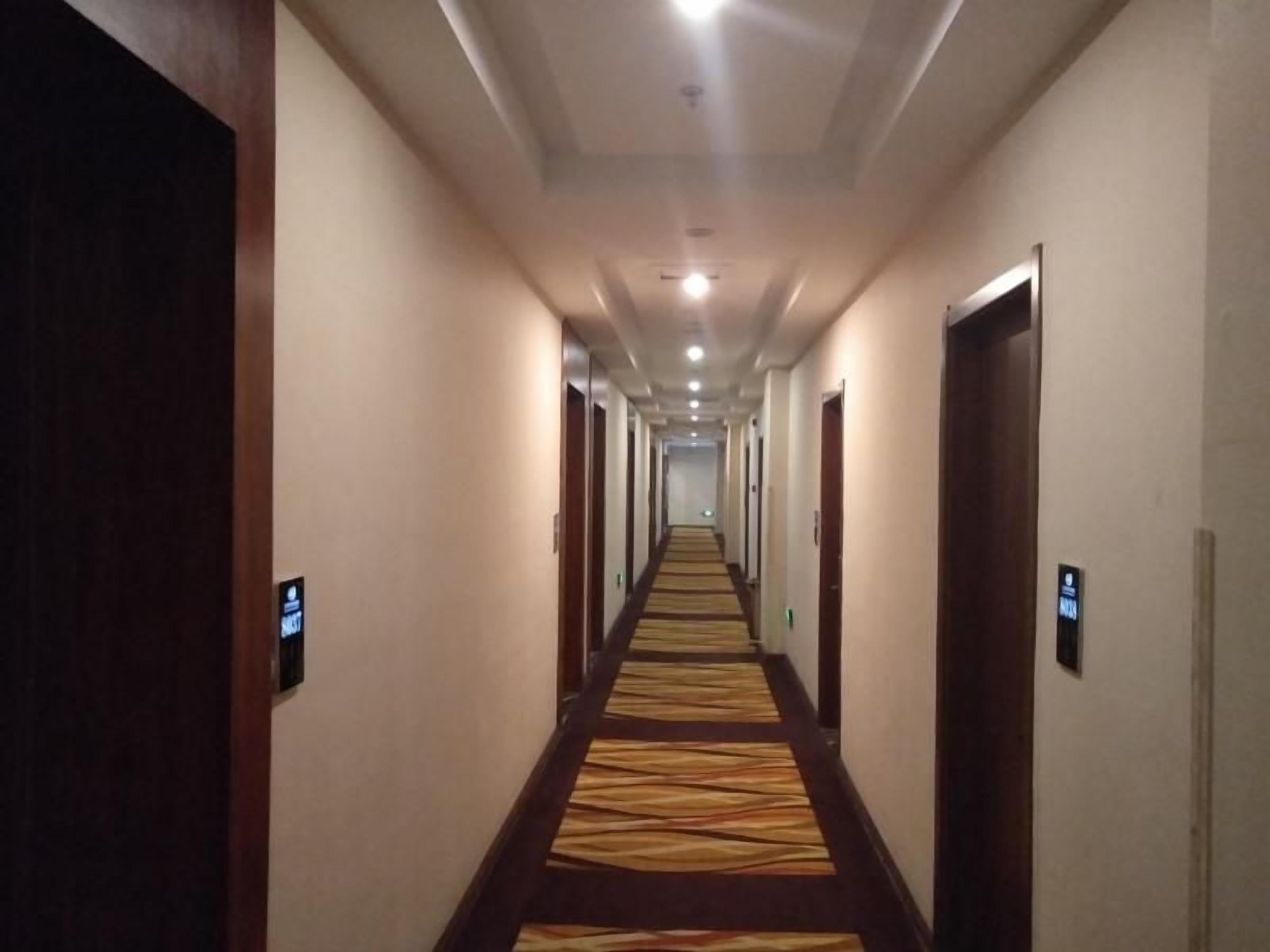 A hotel hallway with carpeted floors, doors on both sides, and a long corridor leading to a bright end.