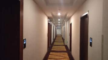 A hotel hallway with carpeted floors, doors on both sides, and a long corridor leading to a bright end.