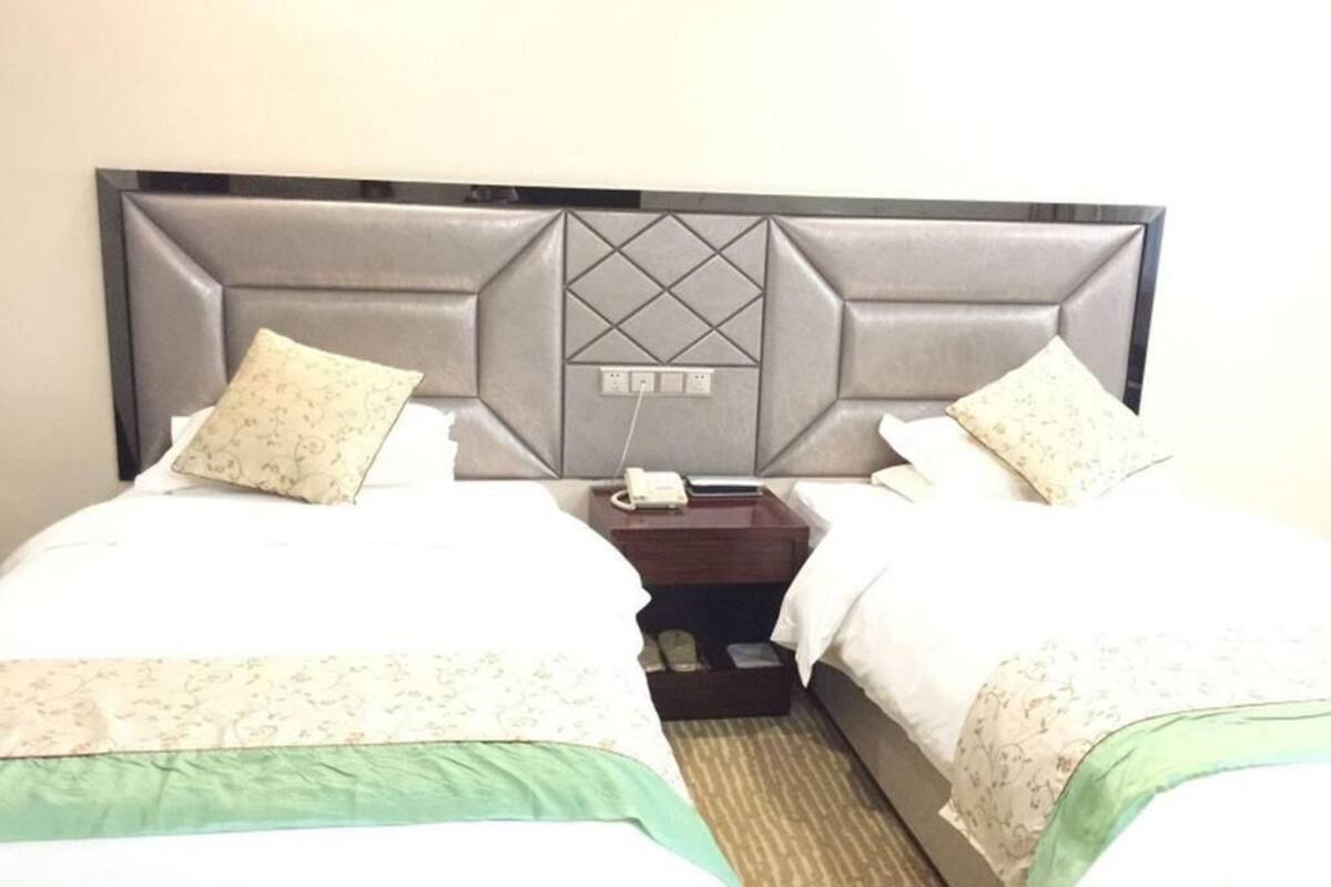 Une chambre d’hôtel avec deux lits, une tête de lit ornée d’un motif géométrique, une table de chevet avec un téléphone et un petit tiroir.