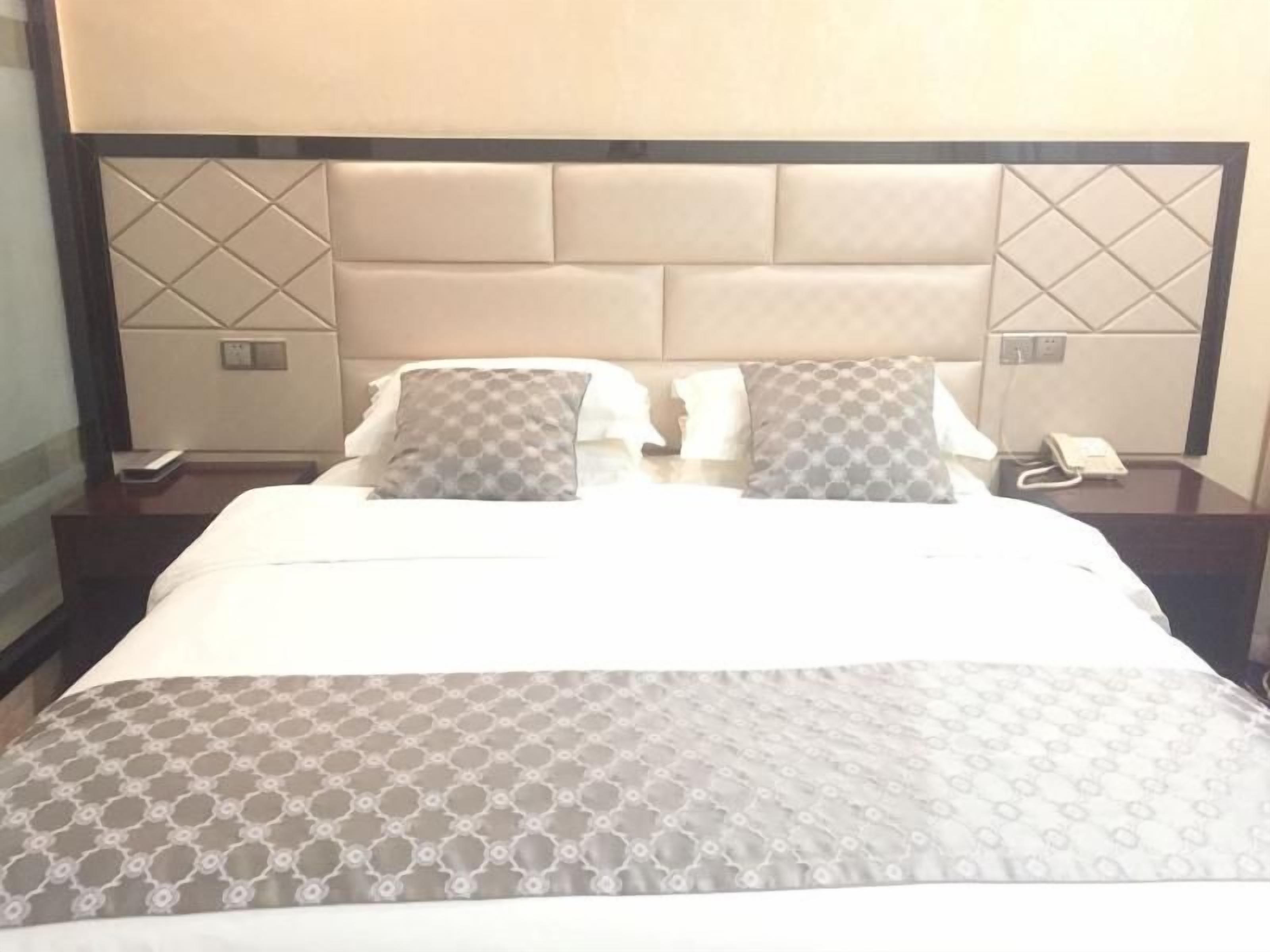 A hotel room with a large bed, two bedside tables, and a headboard with a geometric pattern.