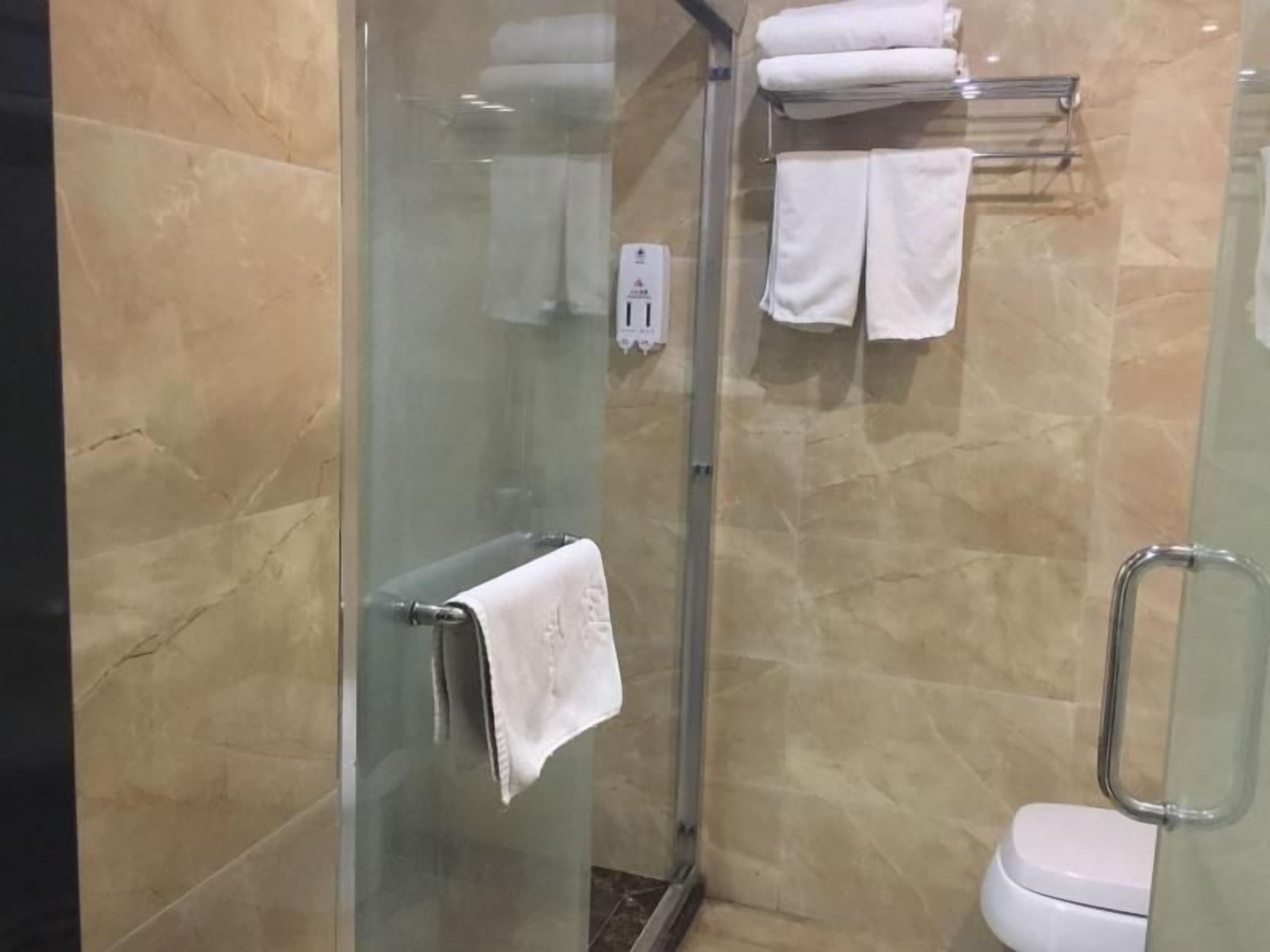 Zona de ducha con paredes de vidrio, un perchero y una toalla blanca colgada en la puerta.