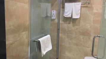 Zona de ducha con paredes de vidrio, un perchero y una toalla blanca colgada en la puerta.