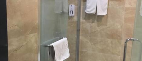 Zona de ducha con paredes de vidrio, un perchero y una toalla blanca colgada en la puerta.