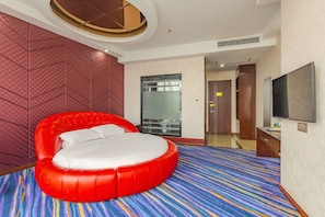 Una habitación de hotel moderna con una cama redonda roja, un televisor de pantalla plana grande y una alfombra colorida a rayas.