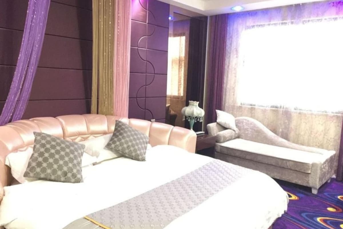 Une chambre d’hôtel avec un grand lit, un canapé, une table de chevet et une fenêtre avec des rideaux.