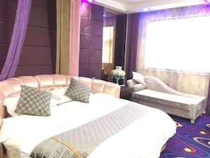 Habitación de hotel con una cama grande, un sofá, un espejo y una ventana con cortinas.