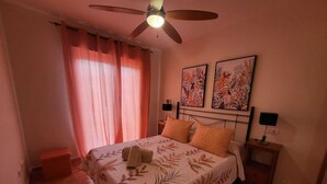 A bedroom with a bed, a ceiling fan, two wall-mounted lamps, and a window with curtains.