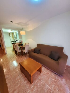A living room with a brown sofa, a wooden coffee table, and a dining area with chairs and a table.