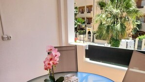 A round glass table with a potted orchid and a white lantern on a balcony with a view of a building and palm trees.