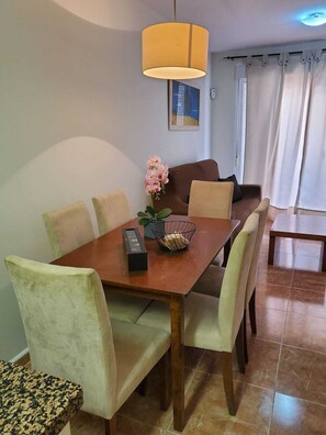 A dining area with a wooden table, cushioned chairs, a remote control, and a flower vase.