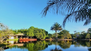 A serene lakeside view with a house, palm trees, and a boat docked near the water. - Vivant Eco Beach OFICIAL (Maraú)
