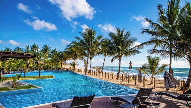 A poolside area with lounge chairs, a wooden deck, and a view of the ocean. - Vivant Eco Beach OFICIAL (Maraú)