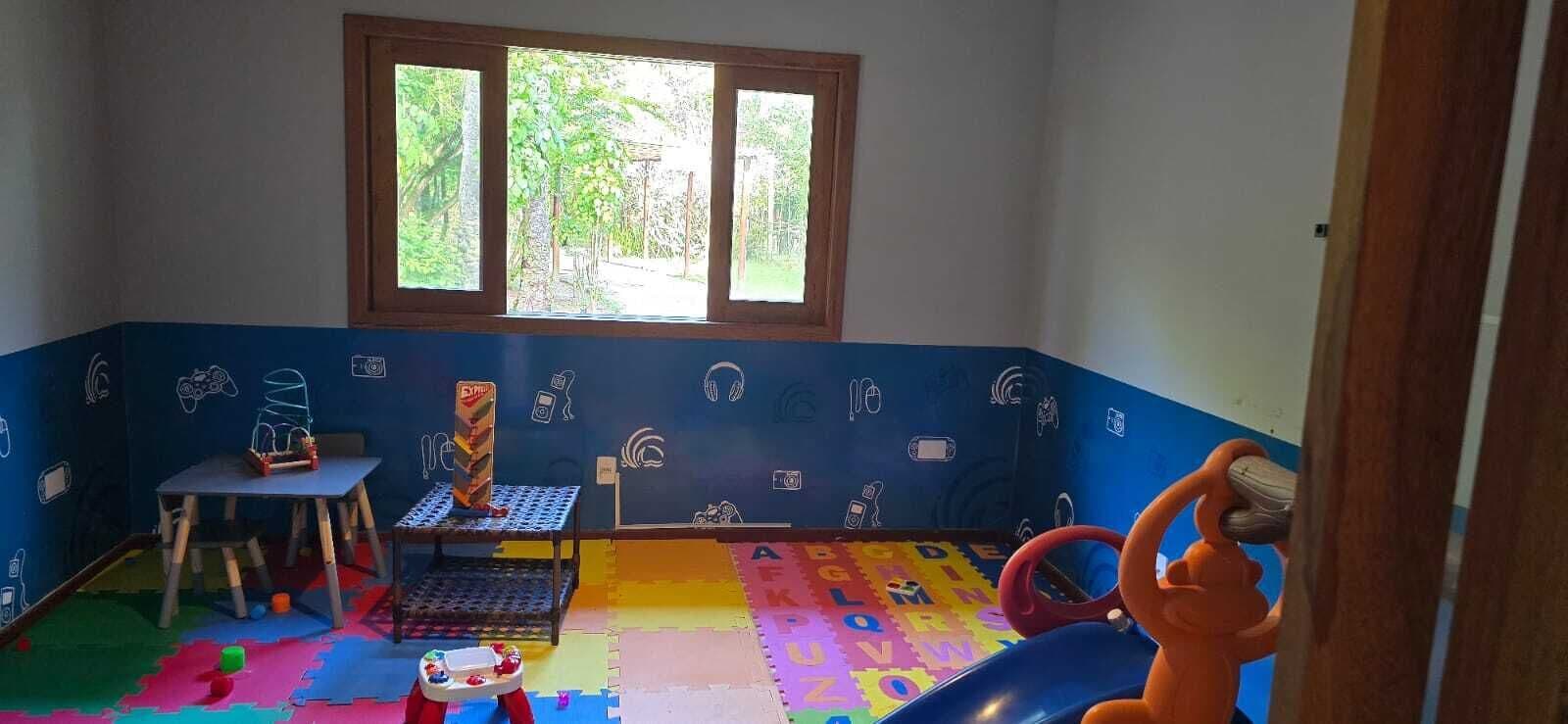 Une salle de jeux pour enfants avec une fenêtre, un tapis de jeu coloré et divers jouets.