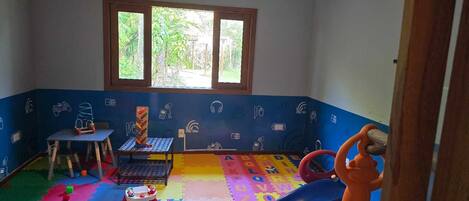 Une salle de jeux pour enfants avec une fenêtre, un tapis de jeu coloré et divers jouets.