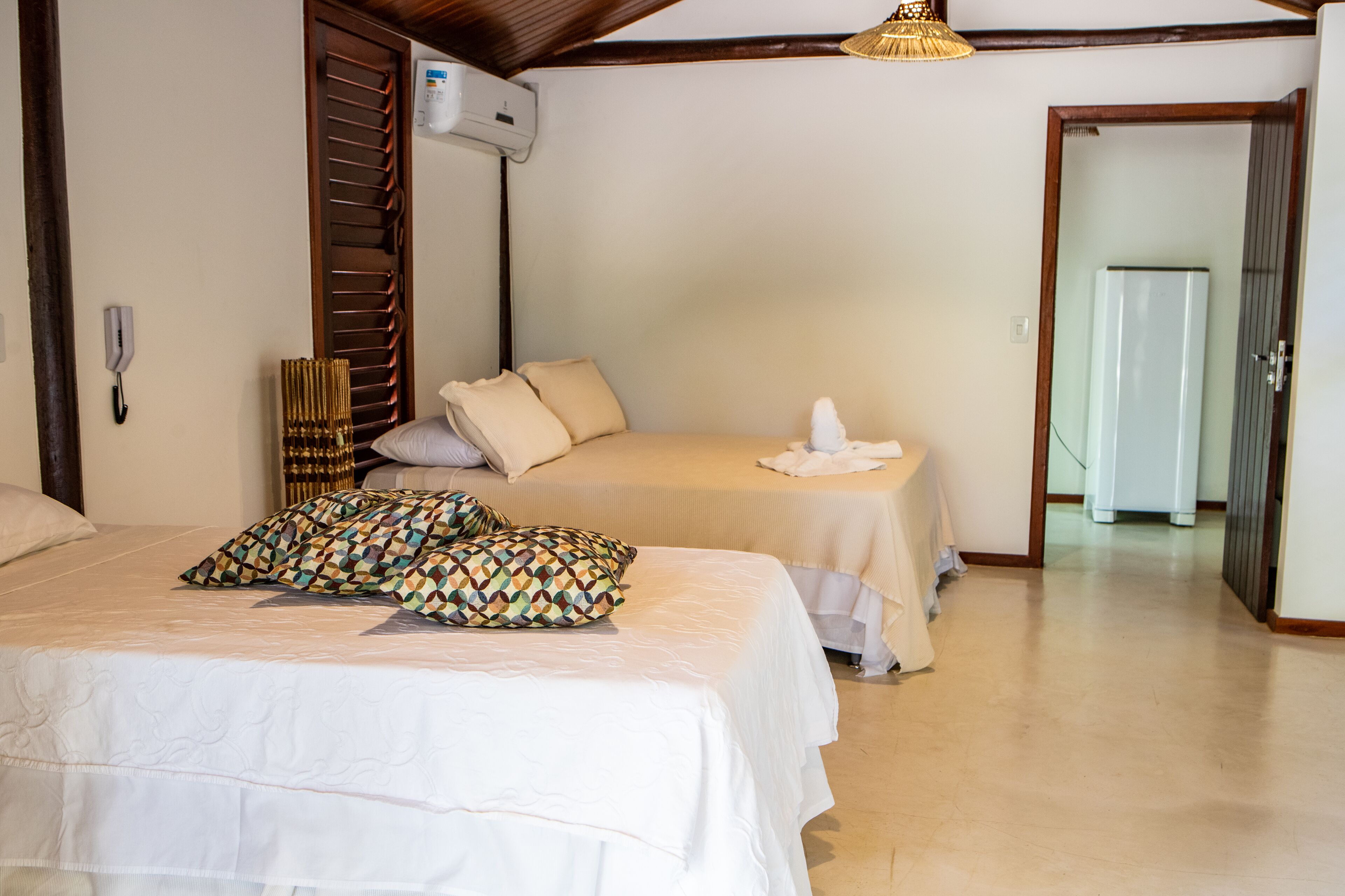 A hotel room with two beds, a telephone, an air conditioning unit, and a doorway leading to another room.