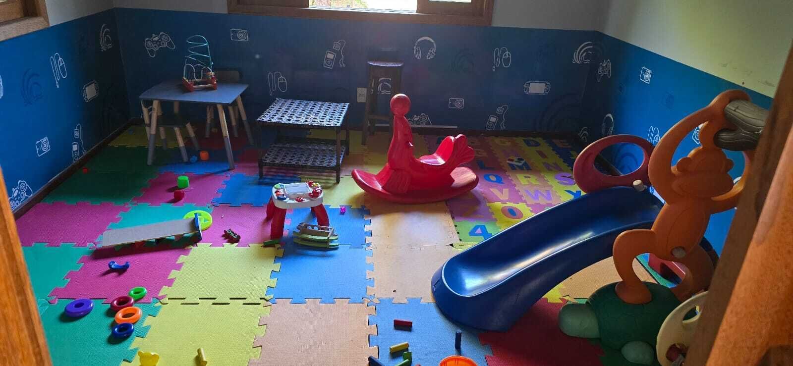 Una sala giochi con tappetini in schiuma colorati, un tavolino, una poltrona a dondolo rossa e uno scivolo blu.