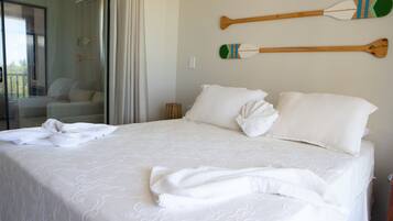 Cama bem arrumada com lençóis e almofadas brancas, decoração de parede com remo de madeira e vista para uma varanda com cadeira.