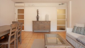 Un salón con una mesa de comedor de madera, sillas, una mesa de centro de vidrio, un sofá y un aparador con objetos decorativos.