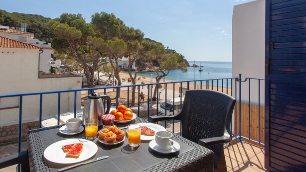 Un balcón con alimentos para el desayuno, vista a la playa y un paisaje costero.