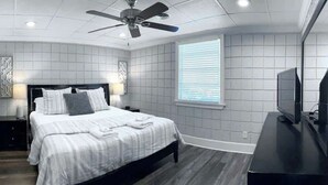 Un dormitorio moderno con cama, ventilador de techo, televisor y ventana con persianas.