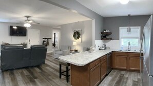 A modern kitchen with a central island, wooden cabinets, and a built-in oven. - The Cottage House - Family Friendly, Close to GSU! (Statesboro)