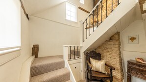 Una escalera con peldaños alfombrados que conduce a un segundo piso, un banco de madera, un pequeño armario de madera y una pared de piedra.