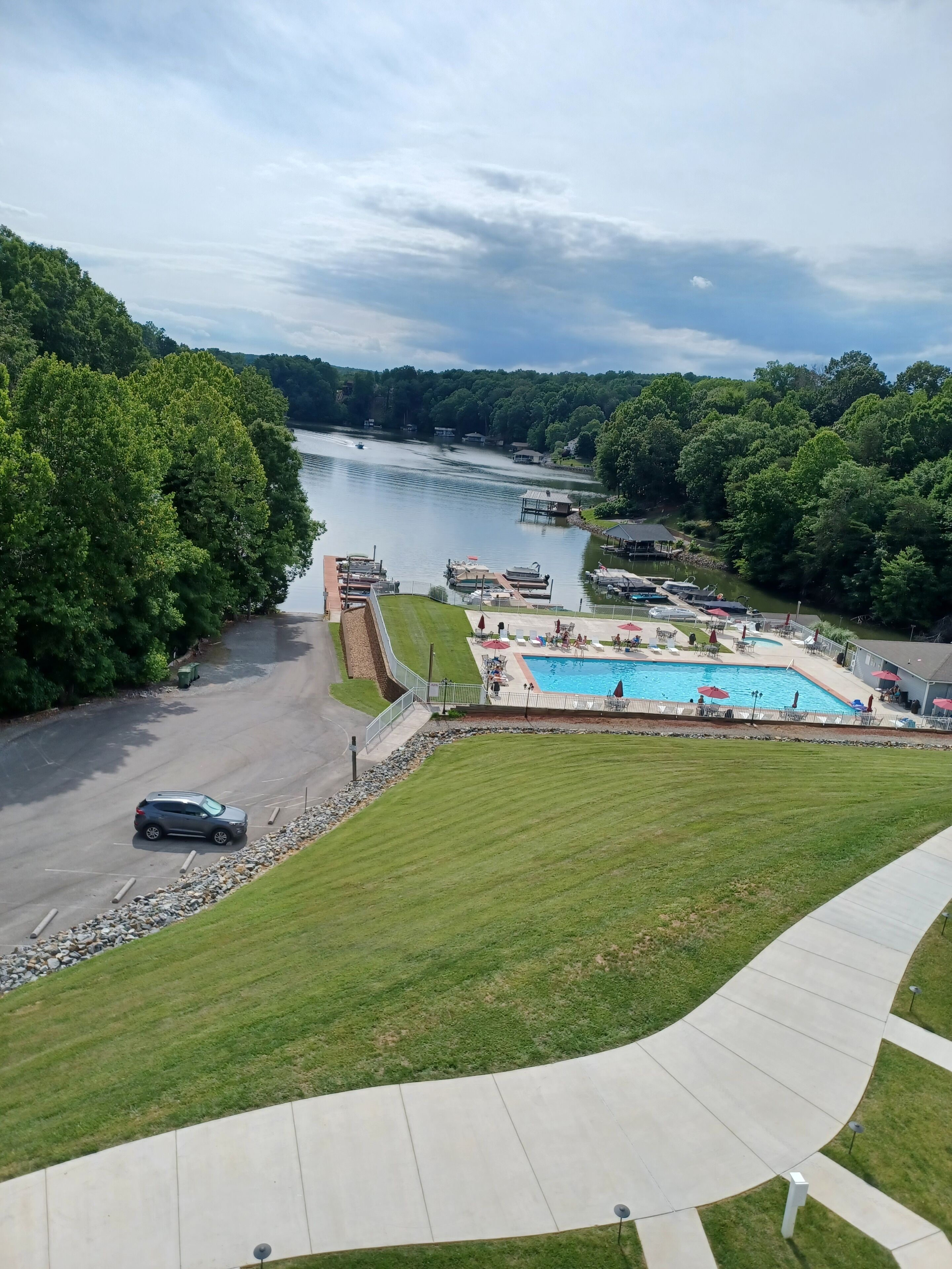 Ein Pool mit Sonnendeck, umgeben von einer Rasenfläche und einem Parkplatz.