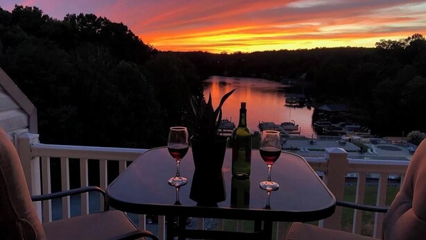 A table with two wine glasses and a bottle, overlooking a body of water and boats at sunset.