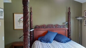 Une chambre à coucher avec un lit à baldaquin, une lampe de chevet et des œuvres d’art encadrées accrochées au mur.