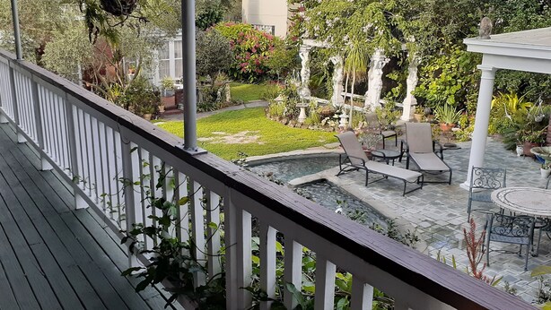 Une terrasse en bois avec une balustrade blanche, un petit jardin agrémenté d’une fontaine et un espace salon extérieur.