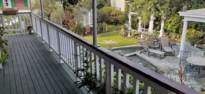 Een houten terras met een witte reling, een kleine tuin met een fontein en buitenmeubels.