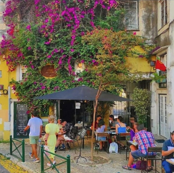 An outdoor café with tables and chairs, surrounded by vibrant bougainvillea flowers.