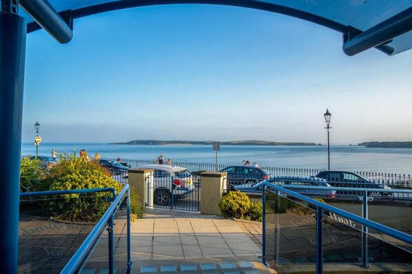 A coastal walkway with a view of the sea, a parking area, and a lamp post.