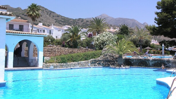 A swimming pool with a stone wall and a blue building with arches. - Refurbished Villa With Private Garden And Large Terraces (Nerja)