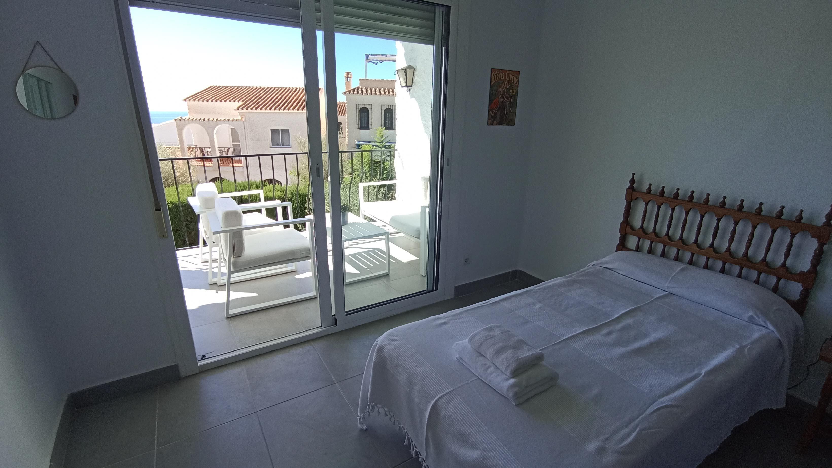 A bedroom with a bed, a sliding glass door leading to an outdoor patio with a table and chairs.