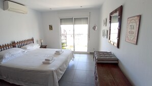 A bedroom with a large bed, a bedside table, a bench, and a window with blinds. - Refurbished Villa With Private Garden And Large Terraces (Nerja)