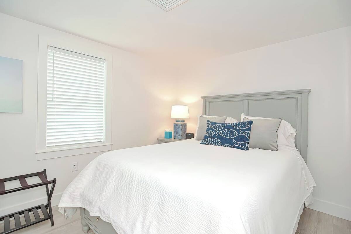 A neatly arranged bedroom with a bed, a bedside table with a lamp, and a window with blinds.
