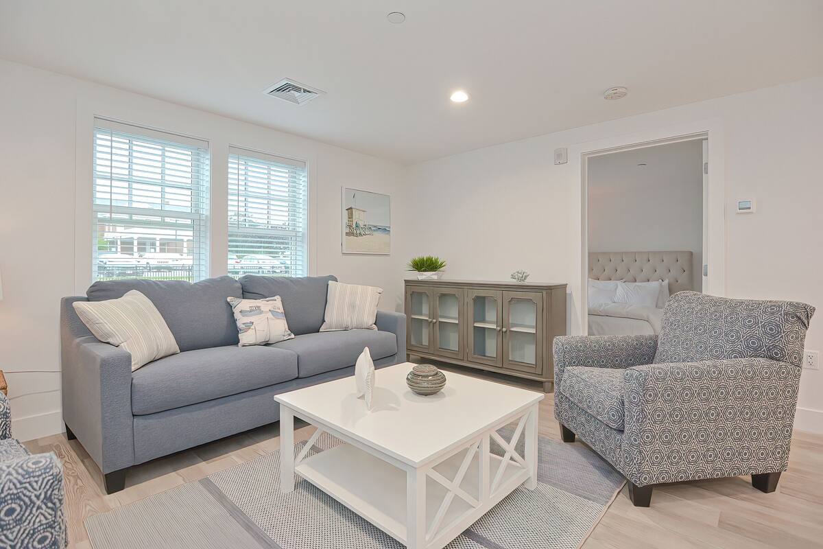 A living room with a grey sofa, a patterned armchair, a white coffee table, and a cabinet with glass doors.