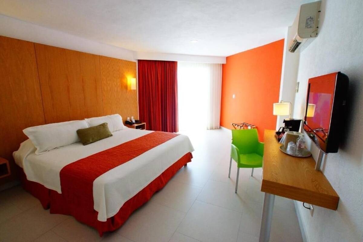 Habitación de hotel con una cama grande, un escritorio con silla, televisor y ventana con cortinas.