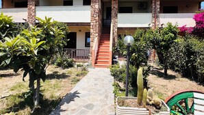A two-story building with a stone column, a red staircase, and a paved walkway leading to the entrance. - Residence La Cinta 7 1P (San Teodoro)
