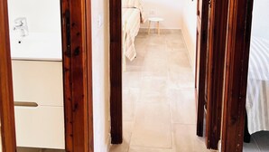 A narrow hallway with wooden doors leading to a bedroom with a bed and a small bedside table. - Residence La Cinta 7 1P (San Teodoro)