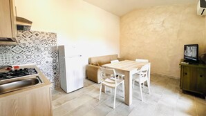 A compact kitchen with a gas stove, a refrigerator, and a dining area with a table and chairs. - Residence La Cinta 7 1P (San Teodoro)