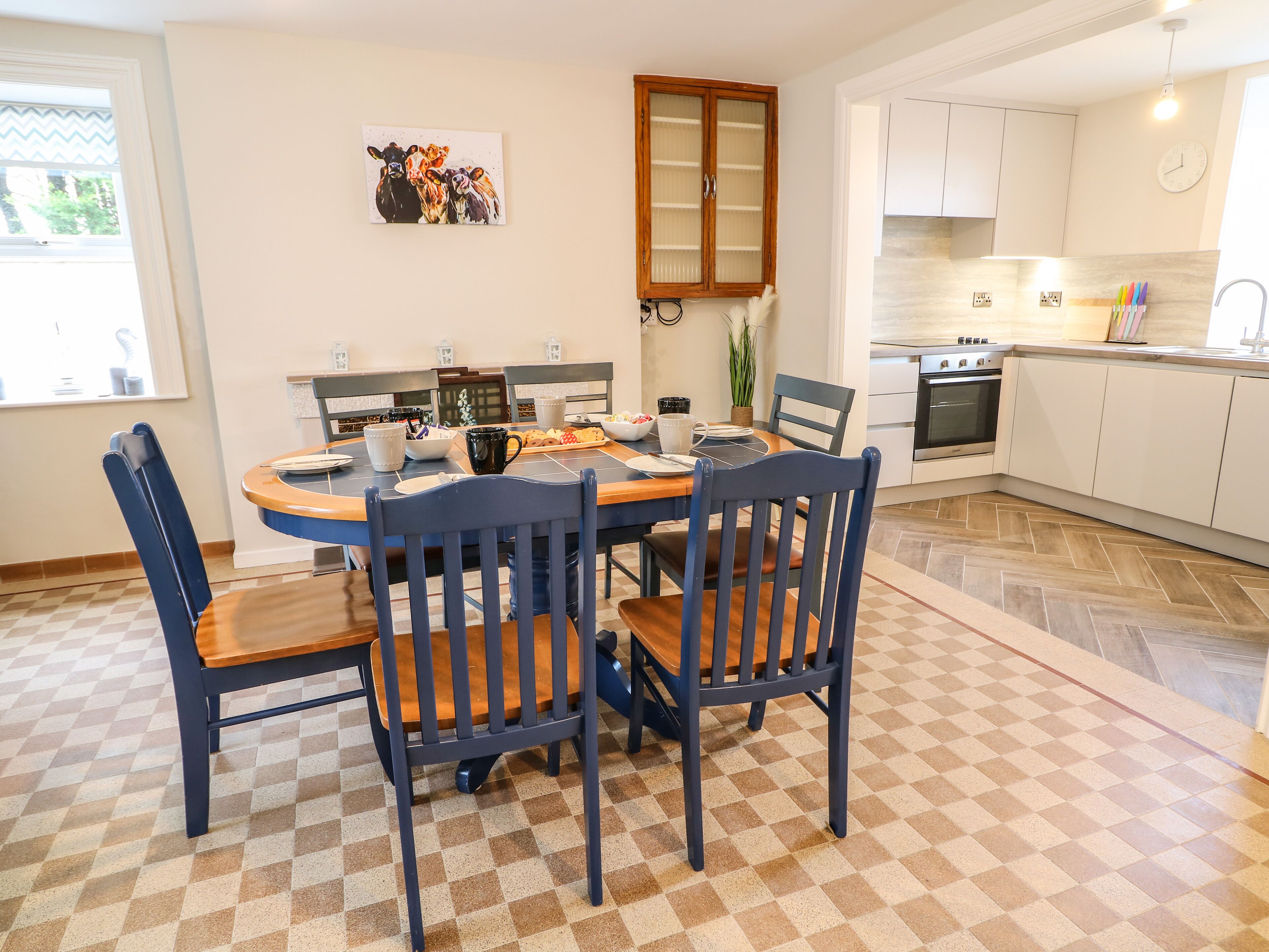 A dining area with a round table, chairs, and a kitchen in the background.