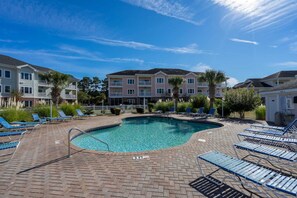 A swimming pool with lounge chairs and a brick patio.