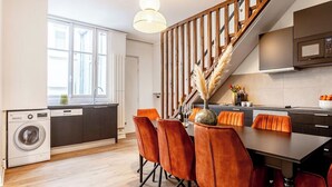 A modern kitchen with a built-in microwave, a dining area with orange chairs, and a staircase leading to another level.
