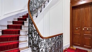 A grand staircase with red carpeted steps, ornate black metal railings, and a wooden door with panels.