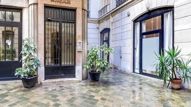 A building with a sign reading 'BUREAUX' and a gated entrance. There are potted plants in front of the doors.