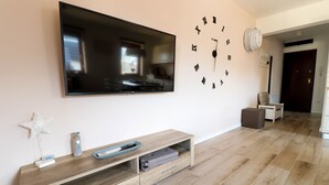 A modern living room with a flat-screen TV mounted on the wall, a wooden entertainment unit below, and a wall clock with Roman numerals. - Old Village House - Holiday Nest (Bohinjska Bistrica)