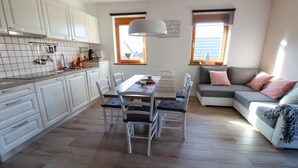 A modern kitchen with white cabinets, a dining table with chairs, and a grey sofa with pink cushions. - Old Village House - Holiday Nest (Bohinjska Bistrica)
